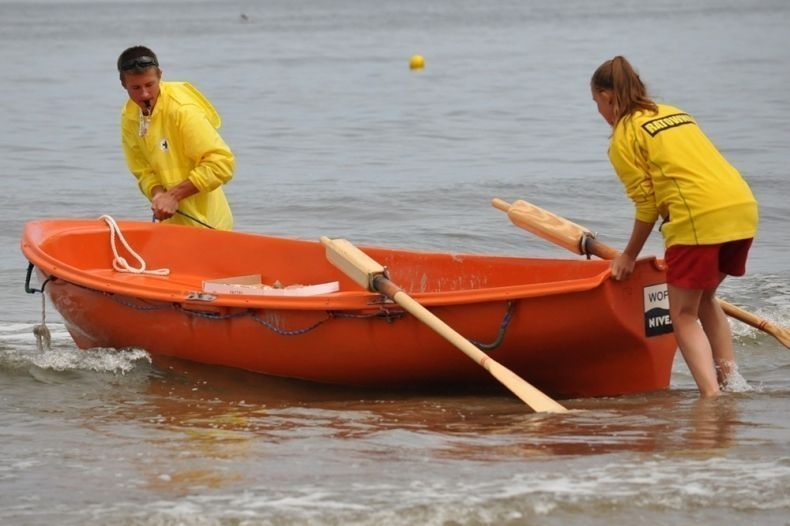 Ratownicy wodni wpychają do wody pomarańczową łódź ratowniczą.